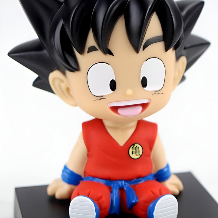 Une figurine de Son Goku, un personnage de Dragon Ball Z, assis sur un socle noir. Il porte une combinaison orange et une ceinture bleue. Il a les cheveux noirs et les yeux bleus. Il sourit.,BO-8449687543