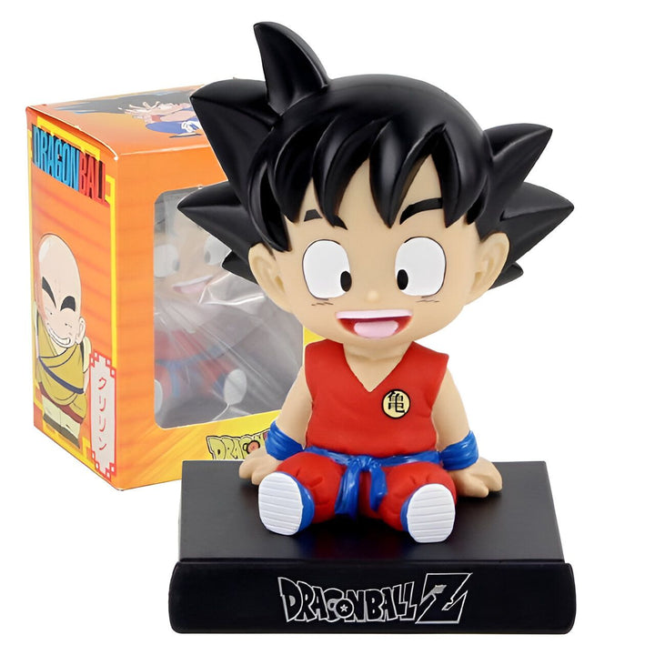 Une figurine de Son Goku, un personnage de Dragon Ball Z, assis sur un socle noir. Il porte une combinaison orange et bleue et a les cheveux noirs hérissés. Il sourit et a les yeux bleus. La figurine est dans une boîte en carton orange et bleue avec une fenêtre transparente.,BO-8449687543