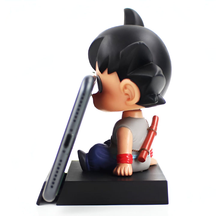Une figurine de Son Goku, un personnage de Dragon Ball Z, est assise sur un socle noir. Il porte une combinaison orange et bleue et tient un téléphone portable dans ses mains.,BO-1118965817