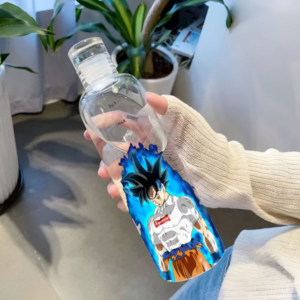 Une bouteille en verre transparente avec un dessin de Son Goku, un personnage de Dragon Ball Z. Son Goku est représenté avec les cheveux bleus et porte un t-shirt blanc avec le logo Supreme. La bouteille est tenue par une main.,BO-4741850803
