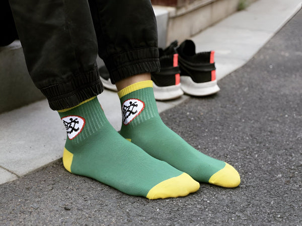 Une personne porte des chaussettes vertes et jaunes avec un motif.,CH-3190135452