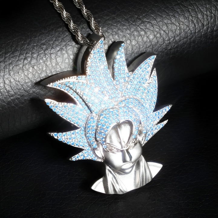 Un pendentif en forme de tête de Goku, un personnage de la série animée japonaise Dragon Ball Z. Le pendentif est en métal argenté et serti de pierres bleues. Il est suspendu à une chaîne en métal argenté.