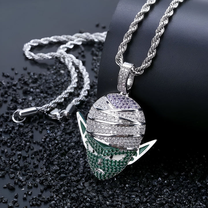 L'image représente un pendentif en forme de tête de Piccolo, un personnage de la série animée Dragon Ball Z. Le pendentif est en argent et serti de pierres précieuses vertes et violettes. Il est suspendu à une chaîne en argent.,CO-5123169970,CO-294831724X