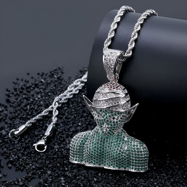 L'image représente un pendentif en forme de personnage de dessin animé, avec une chaîne en argent. Le pendentif est serti de pierres précieuses vertes et blanches.