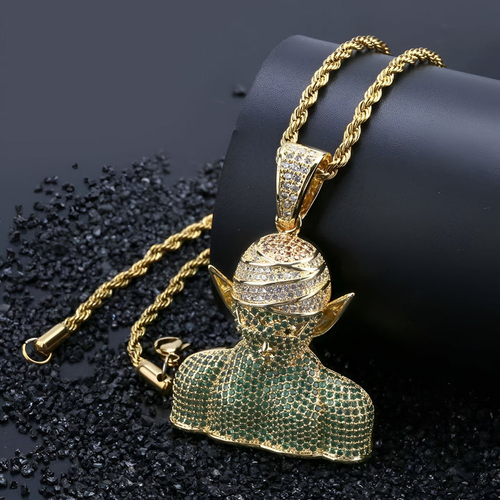 Un pendentif en or avec une chaîne en or. Le pendentif représente le personnage Piccolo de la série Dragon Ball Z. Il est serti de pierres précieuses vertes et blanches.