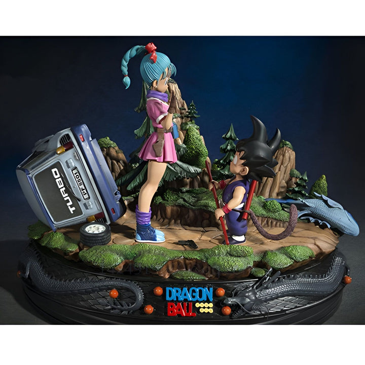Une image de Bulma et Goku, deux personnages de Dragon Ball. Bulma est une jeune femme aux cheveux bleus et Goku est un jeune garçon aux cheveux noirs. Ils sont tous les deux vêtus de combinaisons orange et bleue. Bulma est debout à gauche de l'image et Goku est debout à droite. Il y a une voiture bleue renversée entre eux. Derrière eux, se trouve un paysage montagneux avec des arbres et des rochers.,FI-149907462X