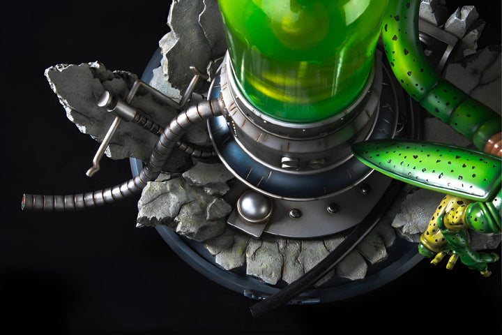 Une image en gros plan d'une figurine de Cell, un personnage de Dragon Ball Z. La figurine est debout sur un socle rocheux et est entourée de tubes et de fils électriques. La figurine est verte et a une longue queue. Le socle est gris et noir.,FI-0653212690