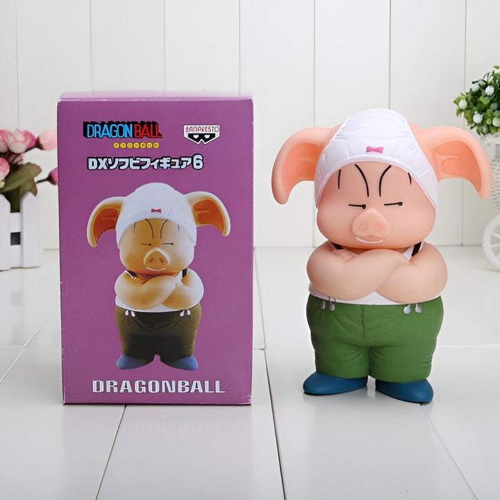 Une figurine de Oolong, un personnage de Dragon Ball, est assise sur une boîte. La figurine est verte et blanche et porte un chapeau blanc. La boîte est rose et blanche et présente le logo de Dragon Ball.,FI-9862983256