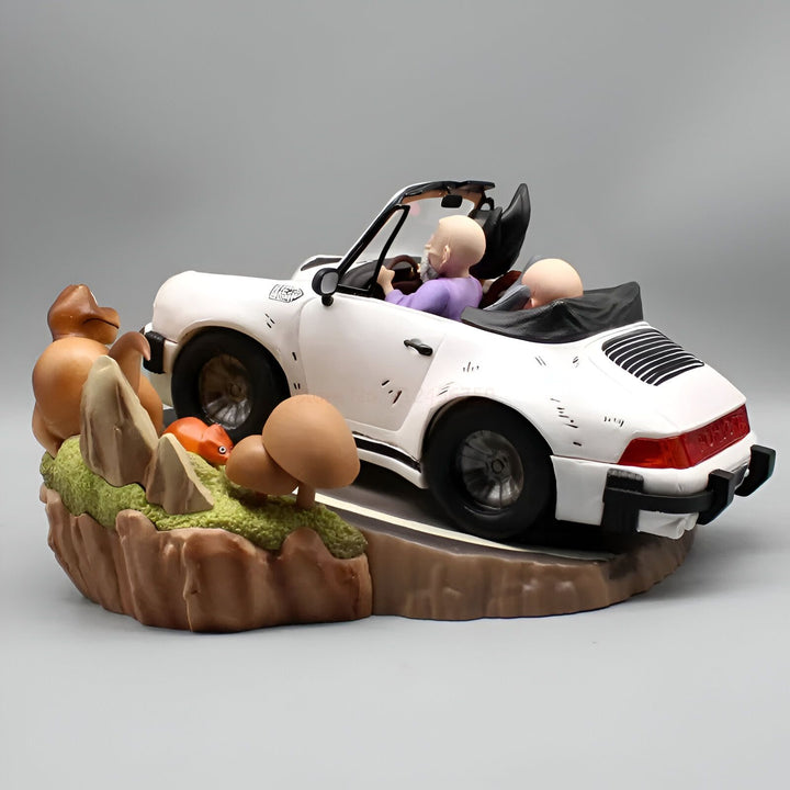 Une image de Tortue Géniale et Krilin dans une Porsche blanche. Tortue Géniale est en train de conduire et Krilin est assis à côté de lui. La voiture est sur une route qui longe une falaise. Il y a des arbres et des rochers sur la falaise.,FI-5159991603