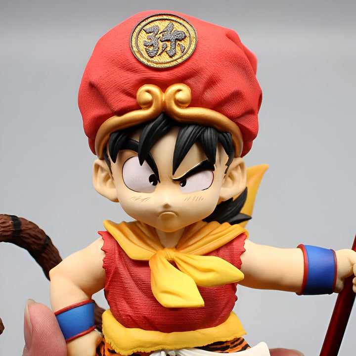 Une figurine de Son Goku enfant portant une tenue traditionnelle chinoise avec un chapeau rouge et une écharpe jaune. Il a les cheveux noirs et les yeux marrons, et tient un bâton dans sa main droite.,FI-4401880579