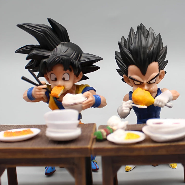 Deux figurines de Dragon Ball Z, Goku et Vegeta, sont en train de manger. Goku est en train de manger un bol de riz avec des baguettes et Vegeta est en train de manger un morceau de viande avec ses mains. Il y a plusieurs assiettes et bols sur la table.,FI-6433225225