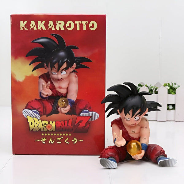 Une figurine de Son Goku, un personnage de Dragon Ball Z, est assise sur une boîte rouge et blanche. Il porte un pantalon orange déchiré et une chemise bleue déchirée. Il a les cheveux noirs et les yeux bleus. Il tient une boule de cristal dans sa main droite.,FI-4324096406