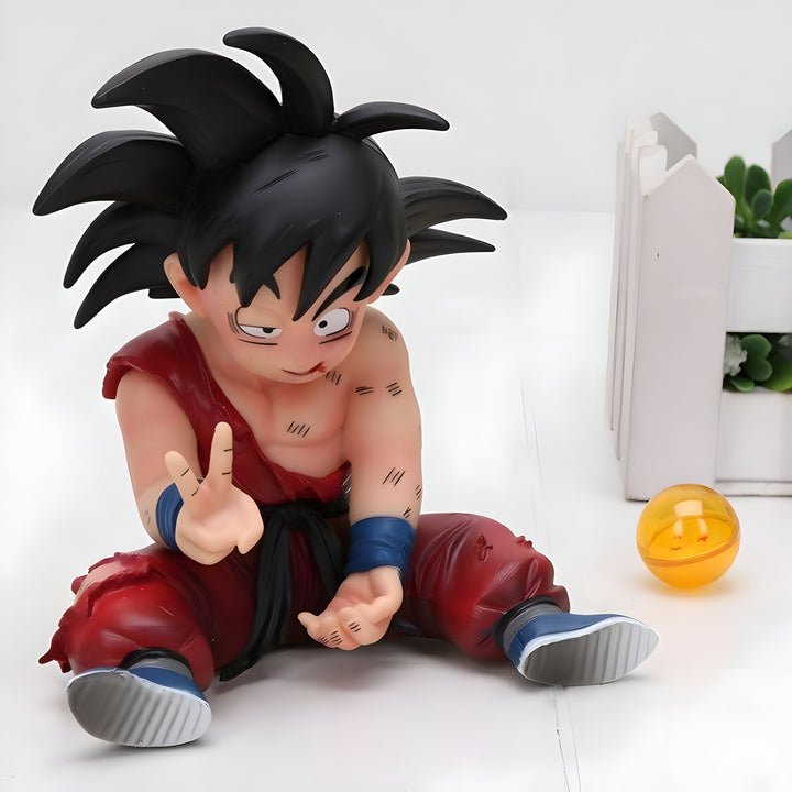 Une figurine de Son Goku, un personnage de Dragon Ball Z, est assise sur le sol. Il a les cheveux noirs, les yeux bleus et porte une combinaison orange et bleue. Il est souriant et fait un signe de la main.,FI-4324096406
