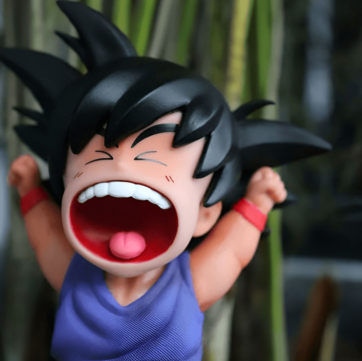 Une figurine de Son Goku, un personnage de Dragon Ball Z, est en train de crier. Il a les cheveux noirs, les yeux bleus et porte une combinaison orange et bleue. Il est entouré de plantes vertes.,FI-1713775565