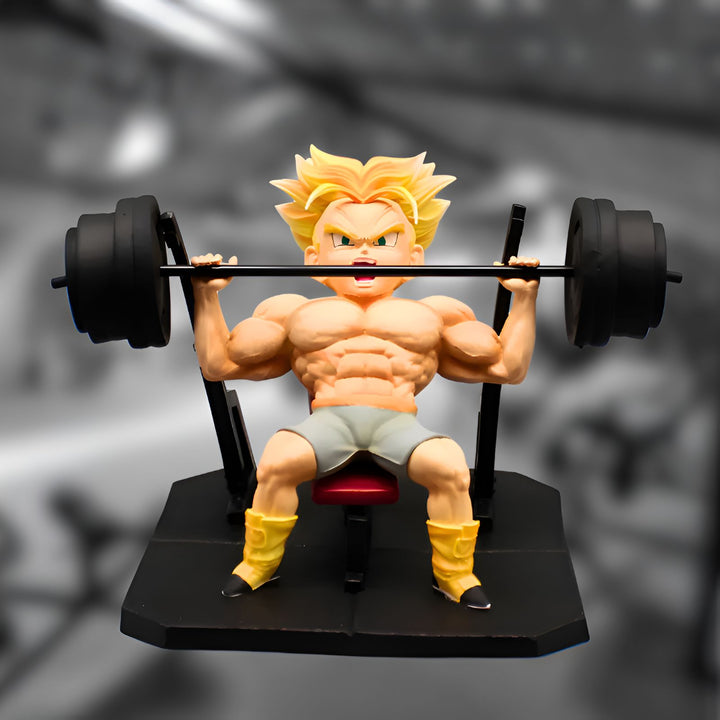 Une figurine de Son Gohan, un personnage de Dragon Ball Z, en train de soulever des poids. Il est assis sur un banc de musculation et porte un short gris et des chaussures jaunes. La figurine est détaillée et montre les muscles de Son Gohan.,FI-9270442446
