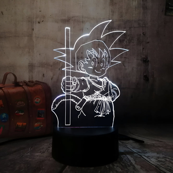 Une image d'un jeune garçon, Son Goku, assis sur un rocher, tenant un bâton à la main. Il a les cheveux hérissés et porte une combinaison orange et bleue. La lumière blanche de la lampe le fait ressortir de l'arrière-plan sombre.,LA-5657397061