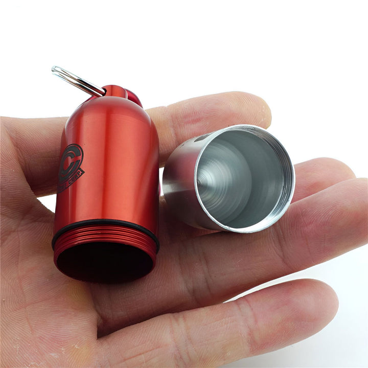 Une main tient une capsule rouge en aluminium de la taille d'un pouce. La capsule est ouverte et on peut voir l'intérieur creux. La capsule est attachée à un porte-clés.,PO-8470058347,PO-3235682589