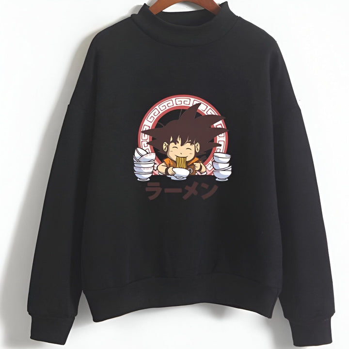 L'image représente un sweat-shirt noir avec un col montant. Sur le devant du sweat-shirt, il y a une image de Son Goku, un personnage de la série animée Dragon Ball Z. Son Goku est en train de manger un bol de ramen. Le texte "ラーメン" (Ramen) est écrit en japonais en rouge dans un cercle rouge et blanc.