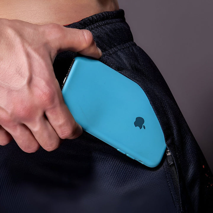 Un homme vêtu d'un short noir et rouge met un téléphone bleu dans sa poche.,SH-2930505052,SH-6989126299,SH-7990178478,SH-3938755318