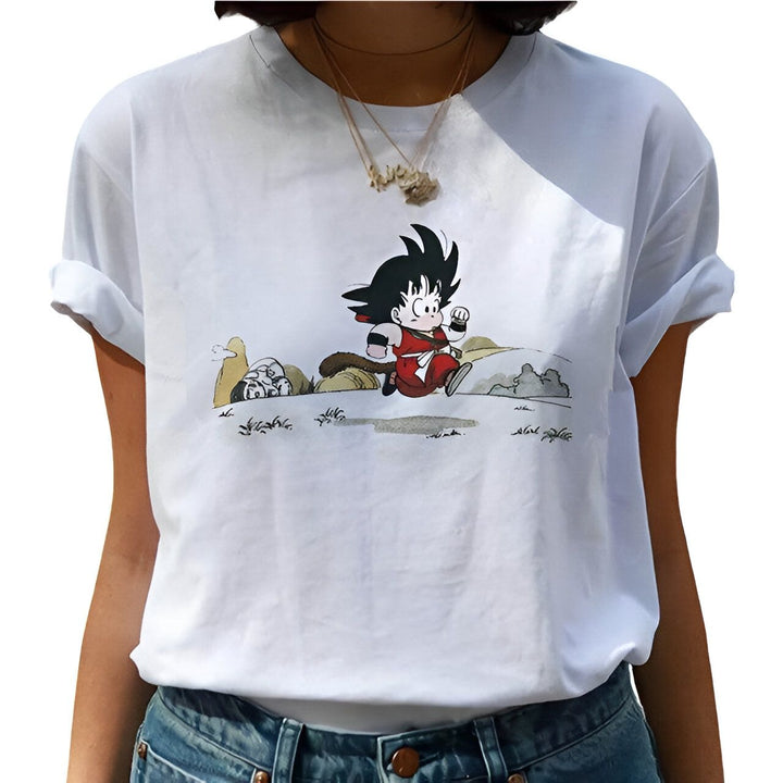 Une jeune femme porte un t-shirt blanc avec un dessin de Son Goku, un personnage de la série animée Dragon Ball Z. Il est représenté en train de courir, avec un air déterminé sur le visage.,T--9040335885,T--5853873059,T--8451299350,T--6012787642,T--8404067600,T--8653936777