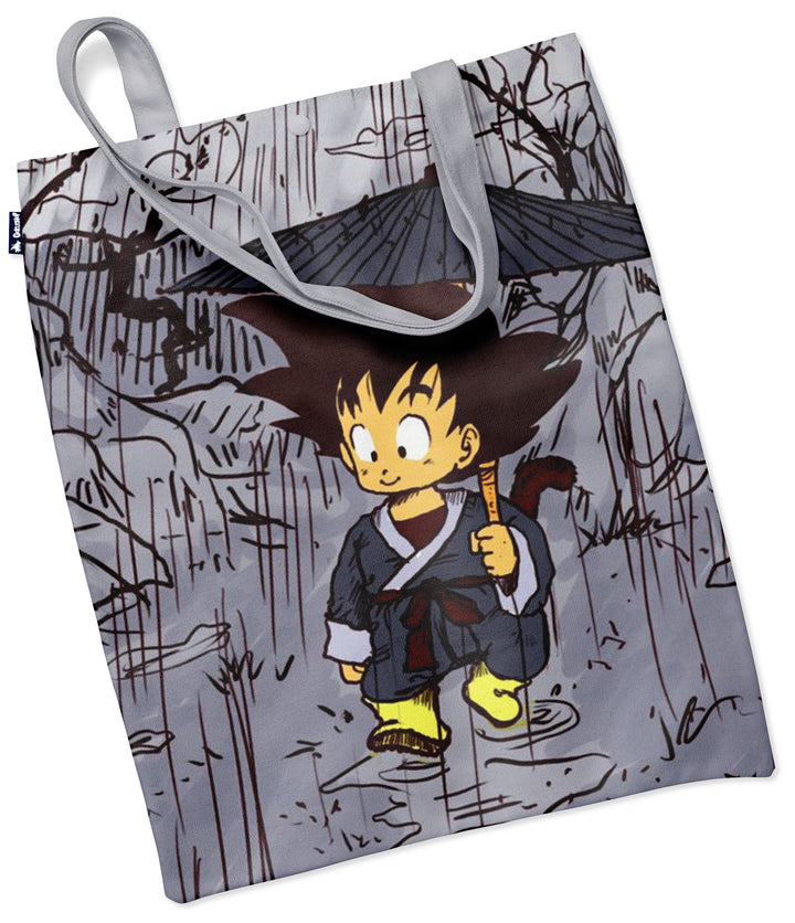 Le tote bag représente le personnage Son Goku, un jeune garçon aux cheveux noirs et aux yeux bleus, vêtu d'un kimono gris et d'une ceinture bleue. Il porte un bâton à la main et se trouve dans un paysage pluvieux.,TO-1103344463